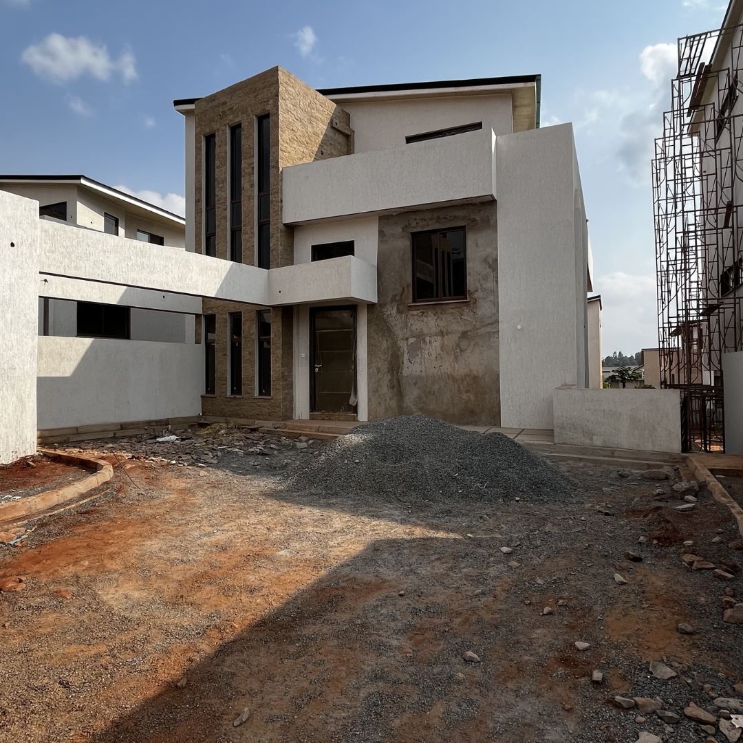 Modern multiunit residential buildings under construction with two story concrete shells and large vertical windows; foreground shows red clay soil, rubble and construction materials indicating an active building site, tone industrious and emerging development
